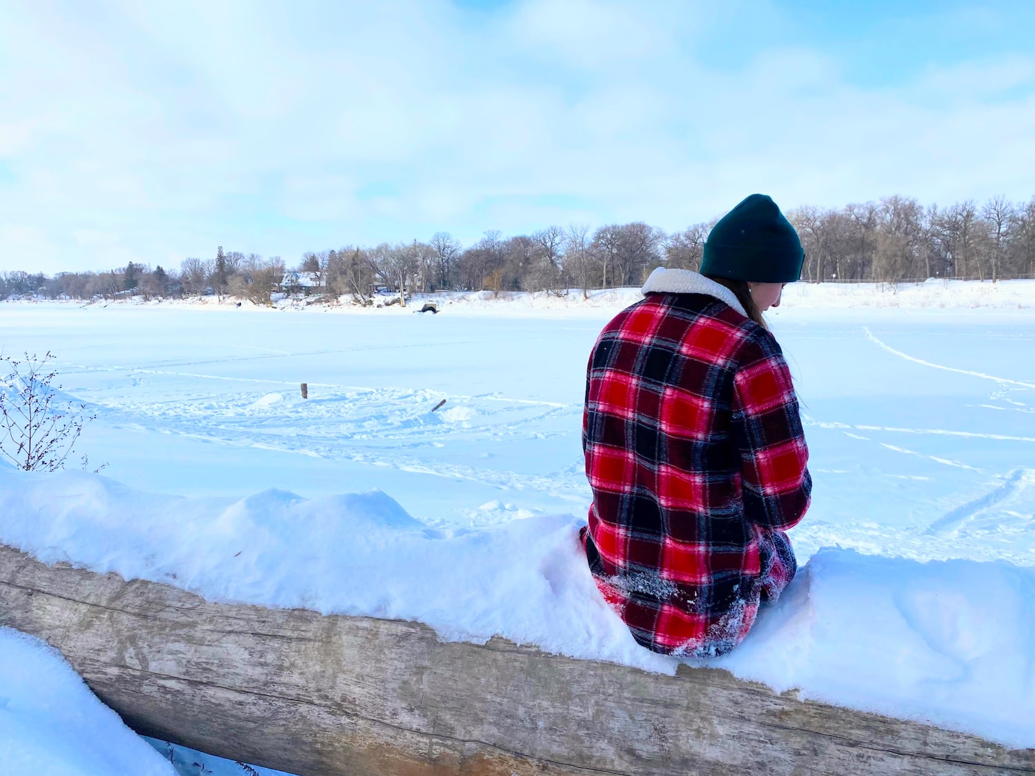 Winter activities in Kelowna. Aly sitting on a log in the snow on the river during winter